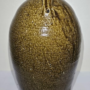 May include: A large, antique stoneware jug with a handle. The jug has a rounded body and a narrow neck. The exterior is glazed in a mottled, earthy brown color with a textured surface. The jug is likely used for storing liquids.