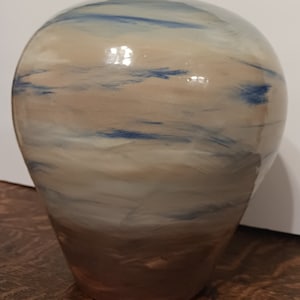 May include: A ceramic vase with a light brown glaze and blue and white streaks. The vase has a rounded top and a narrow base.