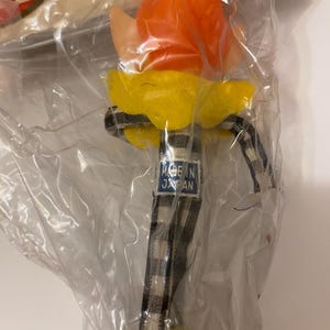 May include: A vintage pixie doll in a clear plastic package. The doll has an orange head, yellow collar, and a black and white checkered stem. The tag reads "MADE IN JAPAN".