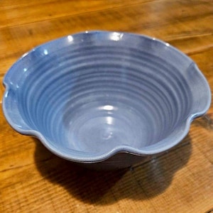 May include: A light blue ceramic bowl with a scalloped rim and a wavy, textured interior. The bowl is empty and appears to be handmade.