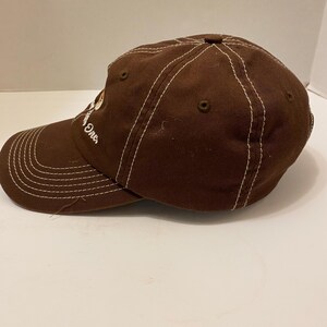 Puede incluir: Gorra de b&eacute;isbol marr&oacute;n con costuras blancas y visera curva. La gorra tiene la palabra "One" bordada en el lateral. El sombrero est&aacute; hecho de una tela duradera y presenta un dise&ntilde;o cl&aacute;sico de seis paneles.