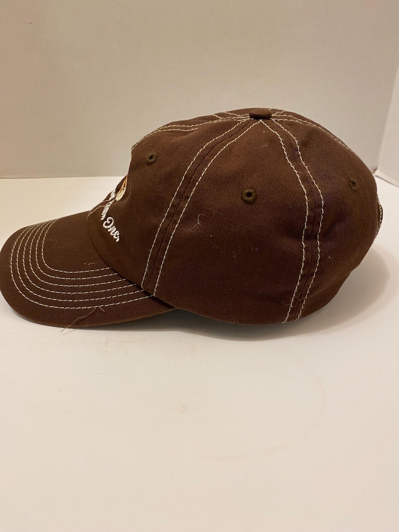 Puede incluir: Gorra de b&eacute;isbol marr&oacute;n con costuras blancas y visera curva. La gorra tiene la palabra "One" bordada en el lateral. El sombrero est&aacute; hecho de una tela duradera y presenta un dise&ntilde;o cl&aacute;sico de seis paneles.