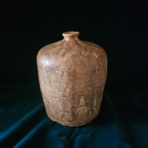 May include: A brown ceramic vase with a textured surface and a slightly flared opening. The vase has a rustic, handmade look.