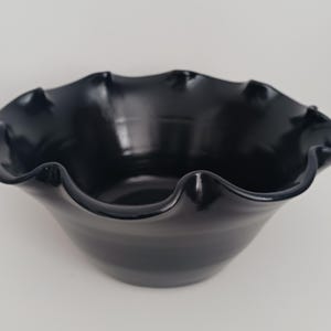 May include: A black ceramic bowl with a ruffled rim. The bowl is glazed and has a smooth, glossy finish.