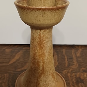 May include: A ceramic candle holder with a brown and tan glaze. The holder has a wide base and a narrow top with a small cup for a candle.