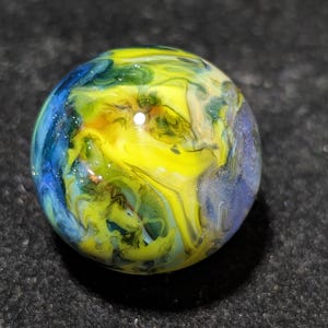 May include: A colorful glass marble with swirling patterns of yellow, blue, and green. The marble is round and has a glossy finish, perfect for collectors or as a decorative item.