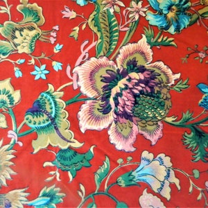 May include: A vibrant floral fabric featuring large, stylized flowers in shades of pink, blue, and yellow against a rich red background. The design includes intricate leaf and vine details, creating a bold and colorful pattern.