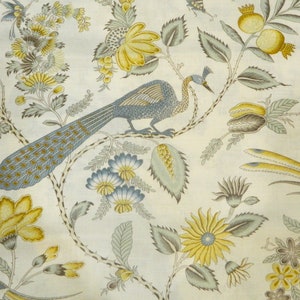 May include: Cream-colored fabric with a repeating pattern of a peacock, flowers, and foliage in shades of blue, yellow, and gray. The peacock is perched on a branch, and the flowers include sunflowers and other stylized blooms.