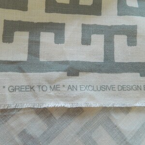 May include: Close-up of fabric with a repeating gray Greek key pattern on a cream background. The text "GREEK TO ME" is printed along the bottom edge. An exclusive design.