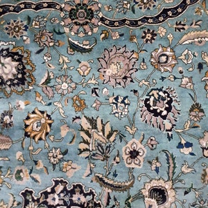 May include: Close-up of a turquoise rug with an intricate floral pattern. The design features various flowers in shades of gray, beige, and blue, with dark blue border accents. The rug has a soft, textured appearance.