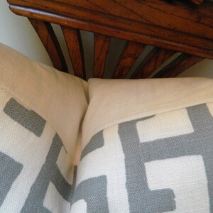 May include: Two decorative throw pillows with a white background and a gray geometric pattern. The pillows are rectangular and have a light-colored border. A wooden decorative element is visible in the background.