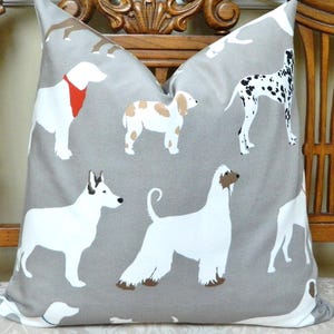 May include: A decorative throw pillow with a gray background featuring various dog breeds in white, brown, and black. The dogs are in different poses, creating a playful pattern. The pillow is square and appears to be made of fabric.