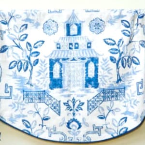 May include: A white valance with a blue Asian-inspired design. The fabric features a repeating pattern of pagodas, trees, and other traditional elements. The valance has a scalloped edge with a dark blue trim.
