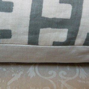 May include: Close-up of a decorative pillow with a geometric pattern. The pillow features a light beige background with a repeating gray block design. The bottom edge has a solid beige border.