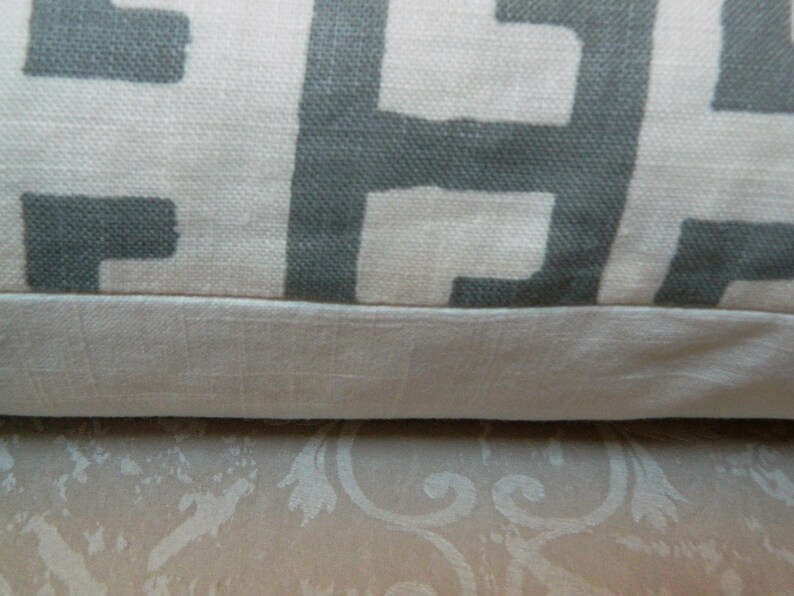 May include: Close-up of a decorative pillow with a geometric pattern. The pillow features a light beige background with a repeating gray block design. The bottom edge has a solid beige border.