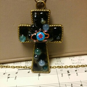 May include: A black cross pendant necklace with a gold chain. The cross is decorated with small, colorful glass beads and a large blue eye in the center.