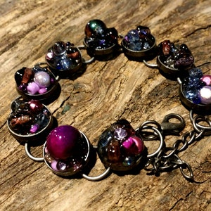May include: A silver bracelet with a chain closure. The bracelet is made of round metal charms, each filled with a variety of colorful beads, including purple, pink, blue, and brown.