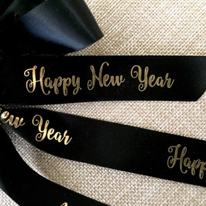 Pu&ograve; includere: Nastro nero con scritta dorata "Happy New Year". Il nastro &egrave; probabilmente utilizzato per confezioni regalo o decorazioni. Lo sfondo &egrave; una superficie strutturata e neutra.