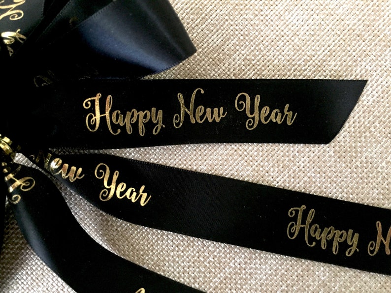 Pu&ograve; includere: Nastro nero con scritta dorata "Happy New Year". Il nastro &egrave; probabilmente utilizzato per confezioni regalo o decorazioni. Lo sfondo &egrave; una superficie strutturata e neutra.