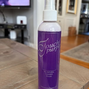 May include: A clear spray bottle filled with a vibrant purple liquid. The bottle has a white spray nozzle and a label that reads "Touch of Purple" and "All Natural Cleaner Polish". The bottle contains 8 fl oz (240 ml) of product.
