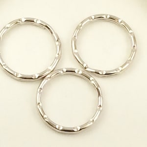 May include: Three silver-colored key rings with a textured, segmented design. The rings are circular and appear to be made of metal. The background is a soft, off-white color, providing a neutral backdrop for the rings.