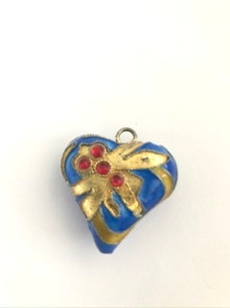 Op de afbeelding: Een blauwe en gouden hartvormige hanger met rode strass steentjes. De hanger heeft een gouden lus aan de bovenkant om aan een ketting te bevestigen.