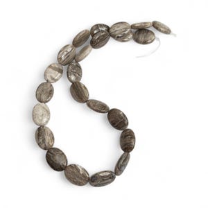 Op de afbeelding: Een ketting van ovale kralen in grijstinten en bruin. De kralen hebben een natuurlijk, gemarmerd uiterlijk en zijn geregen op een wit koord. De ketting wordt gepresenteerd tegen een witte achtergrond.