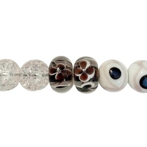 May include: Six decorative glass beads. Two are clear with a crackle effect, two are oval with a dark flower design, and two are white with a dark blue center, resembling eyes. The beads are for jewelry making.
