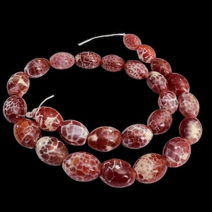 May include: A string of oval beads in red and white, threaded on a white cord. The beads have a marbled effect with a cracked, web-like pattern. The background is black.