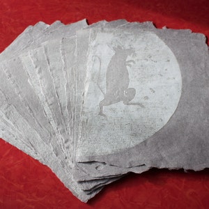 May include: A stack of gray paper with a white silhouette of a rat in the moon on the top sheet.