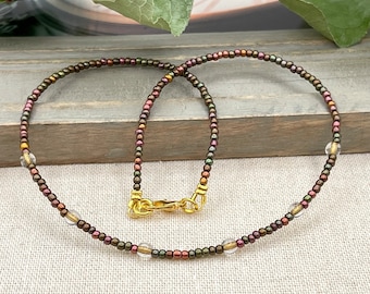 May include: Delicate beaded necklace featuring iridescent dark beads with gold accents and clear crystal beads. The necklace has a gold-colored clasp. A stylish accessory for everyday wear or special occasions.