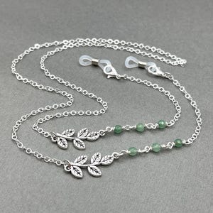 May include: Silver glasses chain featuring leaf charms and green beads. The chain has a delicate design with small links and clear rubber loops for attaching to spectacles. The leaf charms add a natural touch.