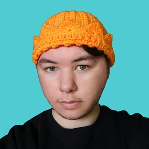 Op de afbeelding: Een persoon draagt ​​een oranje gebreide muts met een kroonontwerp.