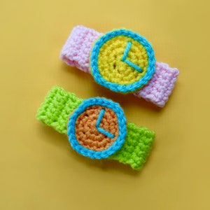 Peut inclure: Deux montres-bracelets en crochet avec des cadrans colorés. Une montre est rose et l'autre est verte.
