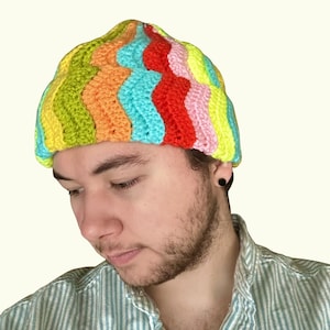 May include: A colorful, handmade crochet beanie in a wavy pattern. The hat features vibrant stripes of yellow, green, orange, turquoise, red, and pink. The beanie is a unique, eye-catching accessory.