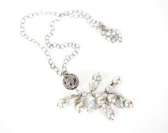 May include: A silver chain necklace with a silver and crystal pendant and a cluster of white pearls.
