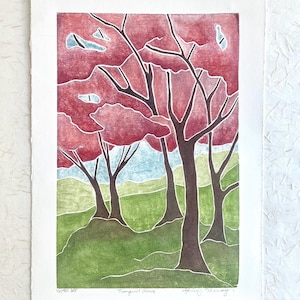 May include: A rectangular art print titled Tranquil Grove featuring a stylized forest scene with dark brown tree trunks, vibrant red foliage, and a green grassy landscape. The print includes the text 16/50 KE, Tranquil Grove, and a signature.