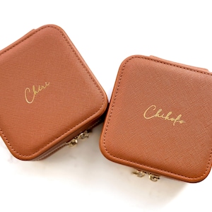 Puede incluir: Dos cajas de joyería de imitación de cuero marrón con letras doradas. La caja de la izquierda dice "Cher" y la caja de la derecha dice "Chihoko".