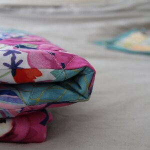 May include: Close-up of a quilted fabric item with a floral pattern in pink, white, and blue. The item is folded, revealing a turquoise interior with gold accents. The stitching is visible.