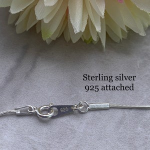 May include: Close-up of a silver chain necklace clasp with the inscription "925" on the clasp. The text "Sterling silver 925 attached" is written above the clasp.