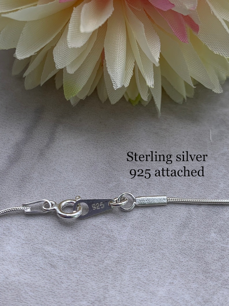 May include: Close-up of a silver chain necklace clasp with the inscription "925" on the clasp. The text "Sterling silver 925 attached" is written above the clasp.