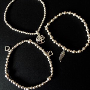 May include: Three silver beaded bracelets with charms. One bracelet has a tree charm, another has a wing charm, and the third has two heart charms.