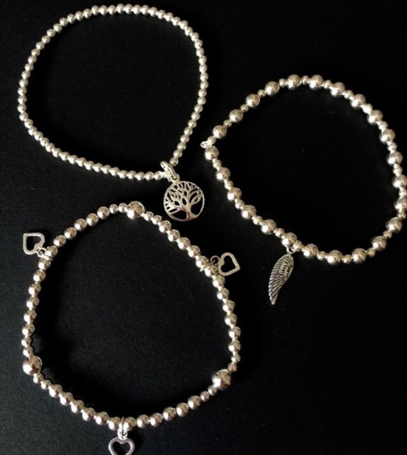 May include: Three silver beaded bracelets with charms. One bracelet has a tree charm, another has a wing charm, and the third has two heart charms.