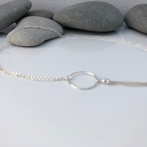 May include: A silver chain necklace with a circle pendant and a small chain tassel.