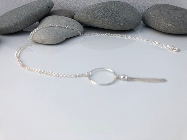 May include: A silver chain necklace with a circle pendant and a small chain tassel.