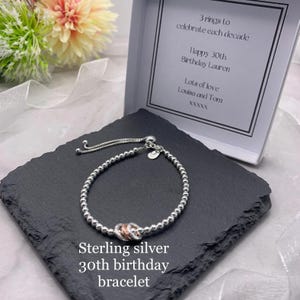 May include: A sterling silver bracelet with three interlocking rings, presented on a black slate. The bracelet is adjustable and features small silver beads. The text on the image reads "Sterling silver 30th birthday bracelet."