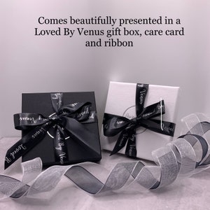 Two gift boxes with black ribbon and white text that reads "Loved By Venus" are shown on a white surface. A black ribbon is wrapped around the boxes.