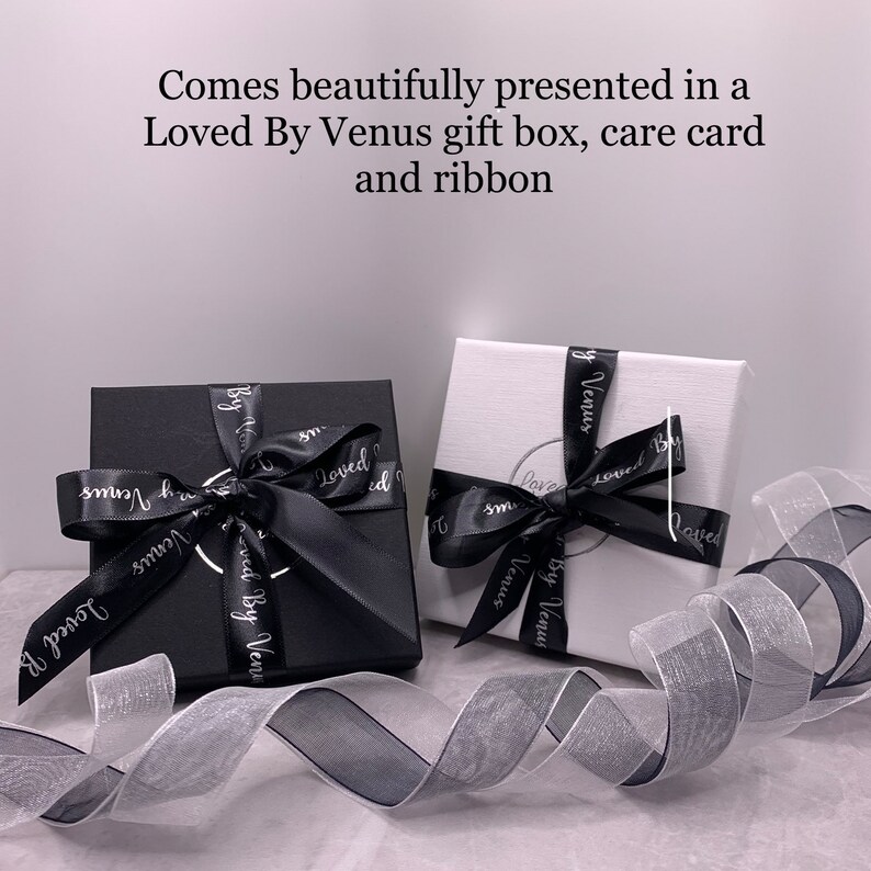 Two gift boxes with black ribbon and white text that reads "Loved By Venus" are shown on a white surface. A black ribbon is wrapped around the boxes.
