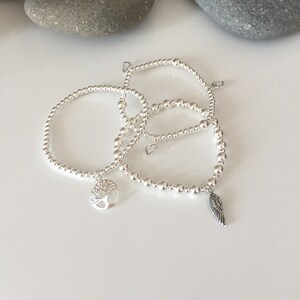 May include: Three silver beaded bracelets with charms. One bracelet has a tree charm, another has a wing charm, and the third has a heart charm.