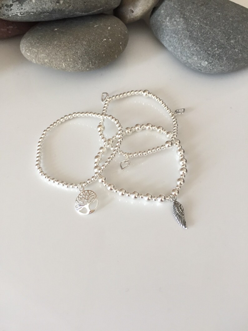 May include: Three silver beaded bracelets with charms. One bracelet has a tree charm, another has a wing charm, and the third has a heart charm.